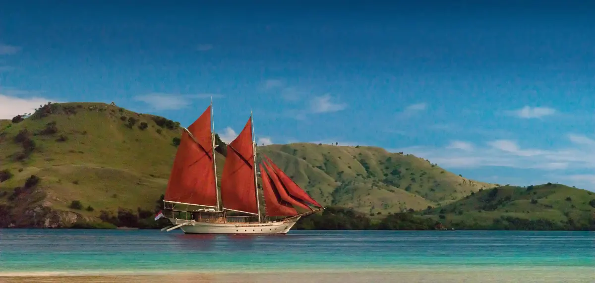Phinisi with red sails off a green island
